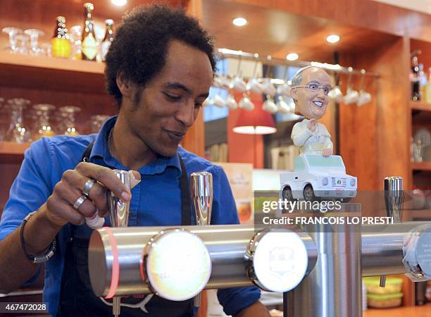 An employee of "Le comptoir de Cana", "a catholic bar" serves a beer next to a figurine depicting Pope Francis, on March 24, 2015 in Lille, northern...