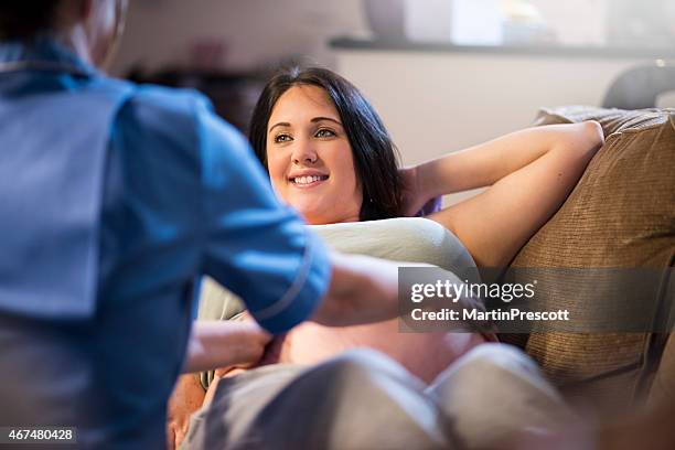 midwife examining pregnant patients abdomen during home visit - mid wife stock pictures, royalty-free photos & images