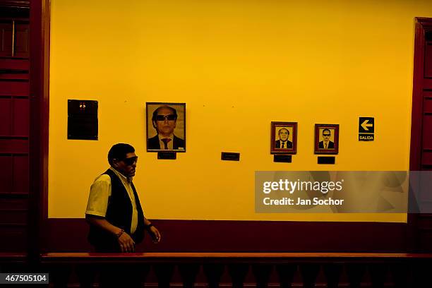 Blind man walks along a corridor with pictures of the club's founders hung on the wall at Unión Nacional de Ciegos del Perú, a social club for the...
