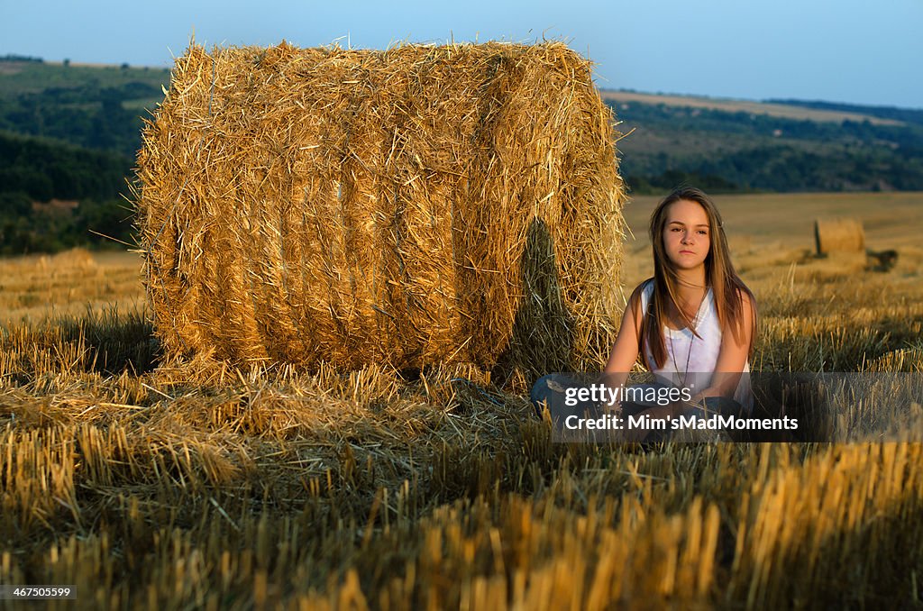 Young girl with blond hair, round bale and field