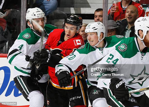 Mikael Backlund of the Calgary Flames gets crunched between Jason Demers and Cody Eakin of the Dallas Stars at Scotiabank Saddledome on March 25,...