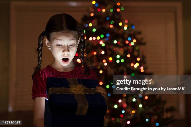 young girl is surprised by a bright christmas gift - christmas surprise stock pictures, royalty-free photos & images