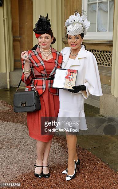Dame Joan Collins holds her insignia of Dame Commander of the British Empire next to her daughter Tara Newley after being awarded by the Prince of...