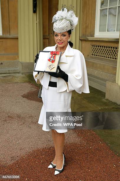 Dame Joan Collins holds her insignia of Dame Commander of the British Empire after being awarded by the Prince of Wales at an Investiture Ceremony at...