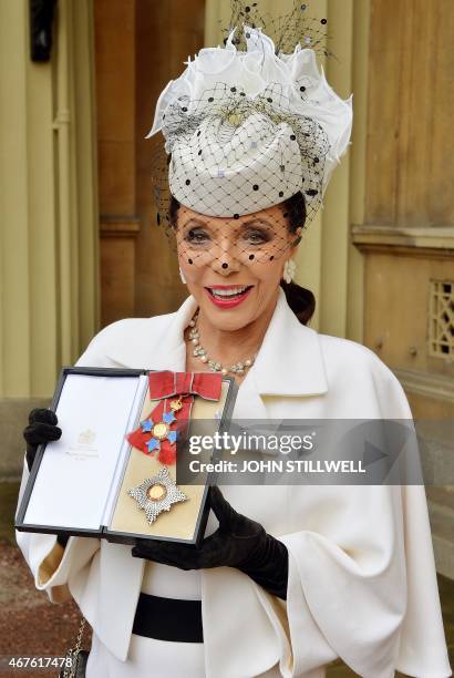 British actress Joan Collins poses for pictures as she holds her insignia of Commander of the Order of the British Empire, after it was awarded to...