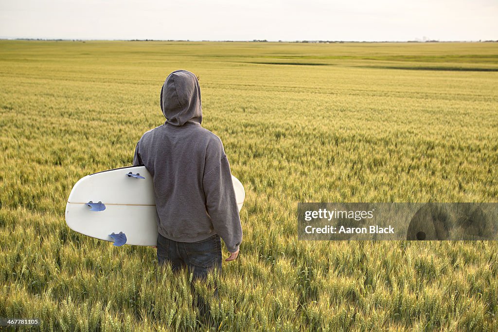 Surfer with a surfboard in an ocean of wheat