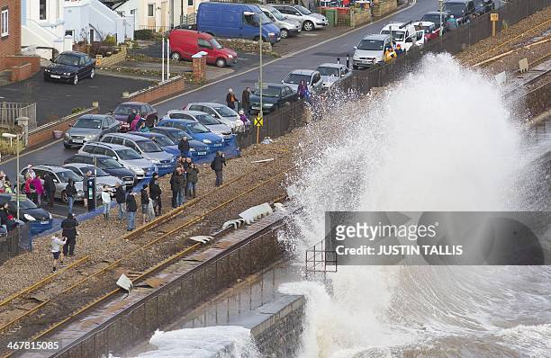 People stand on the storm-damaged main Exeter to Plymouth railway line to watch waves crash onto the shore during high tide in Dawlish on February 8,...