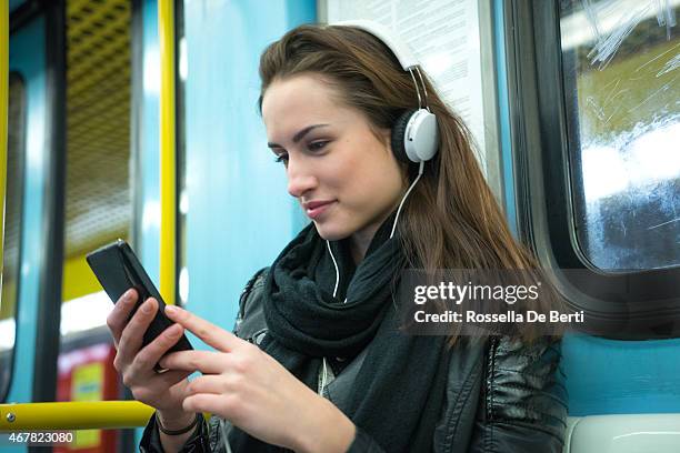smiling woman listening to music on smart phone in subway - portability stock pictures, royalty-free photos & images