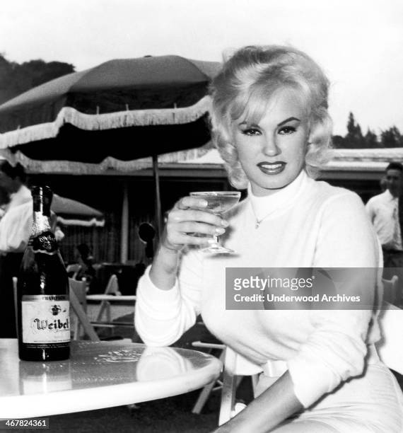 Sultry Mamie Van Doren enjoys a glass of champagne at a Hollywood brunch honoring the completion of 'The Private Lives Of Adam And Eve,' in which she...