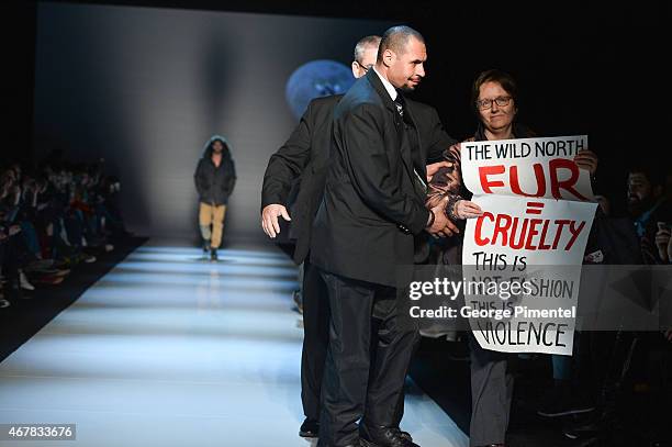 Security escorts a protester holds an anti-fur off the runway during the show for The Wild North fall 2015 collection during World MasterCard Fashion...
