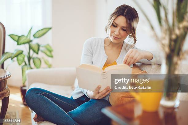 schöne latin frau liest ein buch wie zu hause fühlen - relaxing sofa stock-fotos und bilder