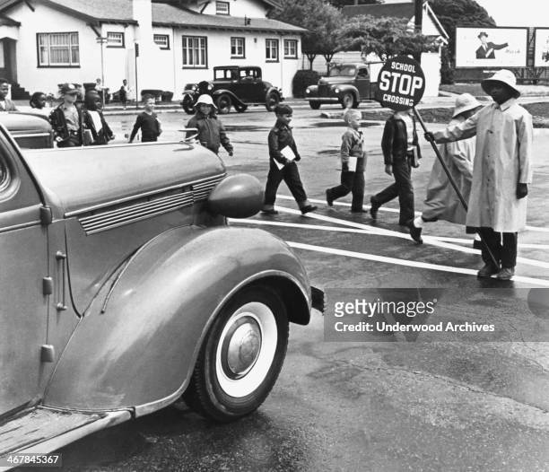 School crossing guard holds a stop sign to halt traffic for children, Berkeley, California, mid to late 1940s.