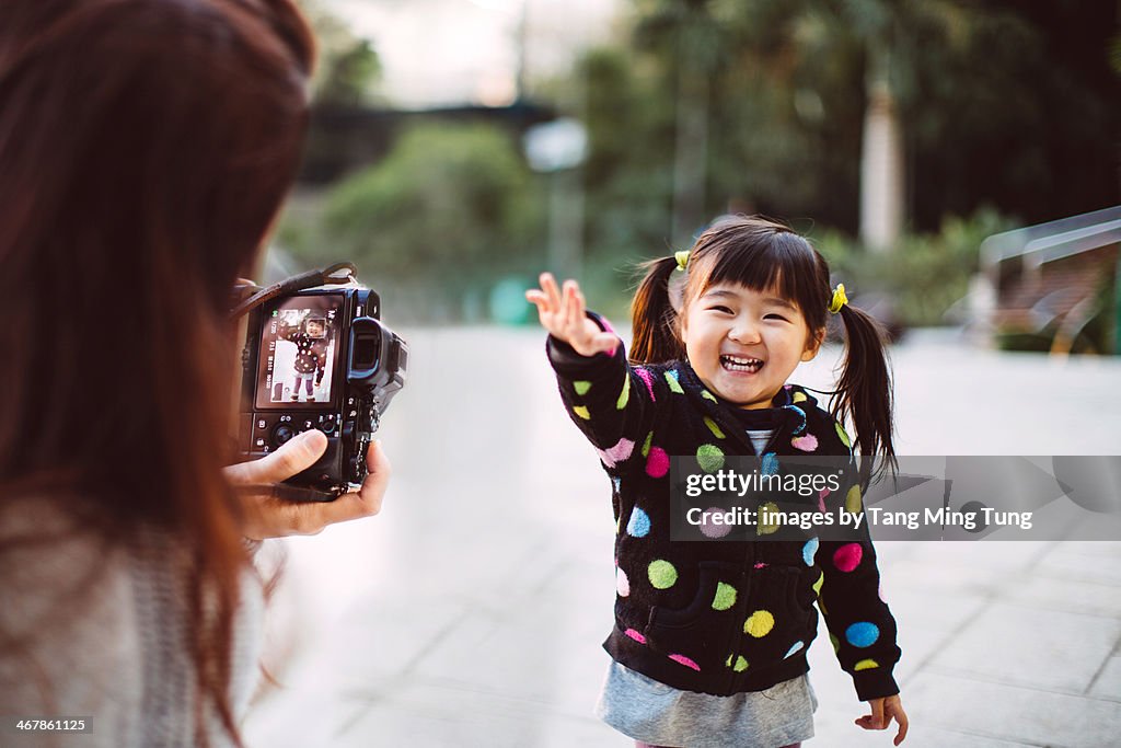 Mom taking picture for toddler girl in park