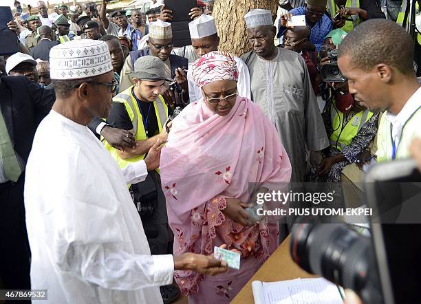 The main opposition All Progressives Congress presidential candidate, Mohammadu Buhari , holds his voter's card to register with his wife, Aisha , on...