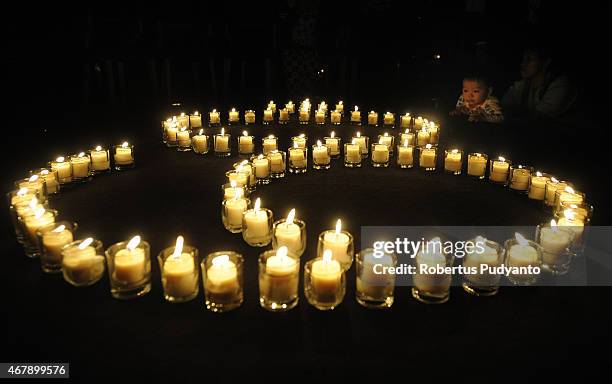 Burning candles displayed in the shape of 60+ during Earth Hour celebration at Sheraton Hotel on March 28, 2015 in Surabaya, Indonesia. Millions of...