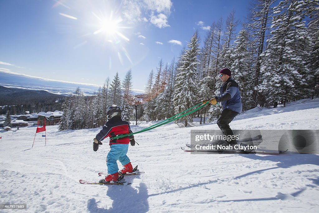 Father teaches and guides son skiing on leash