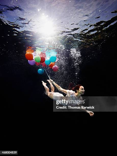 View from underwater of woman holding balloons