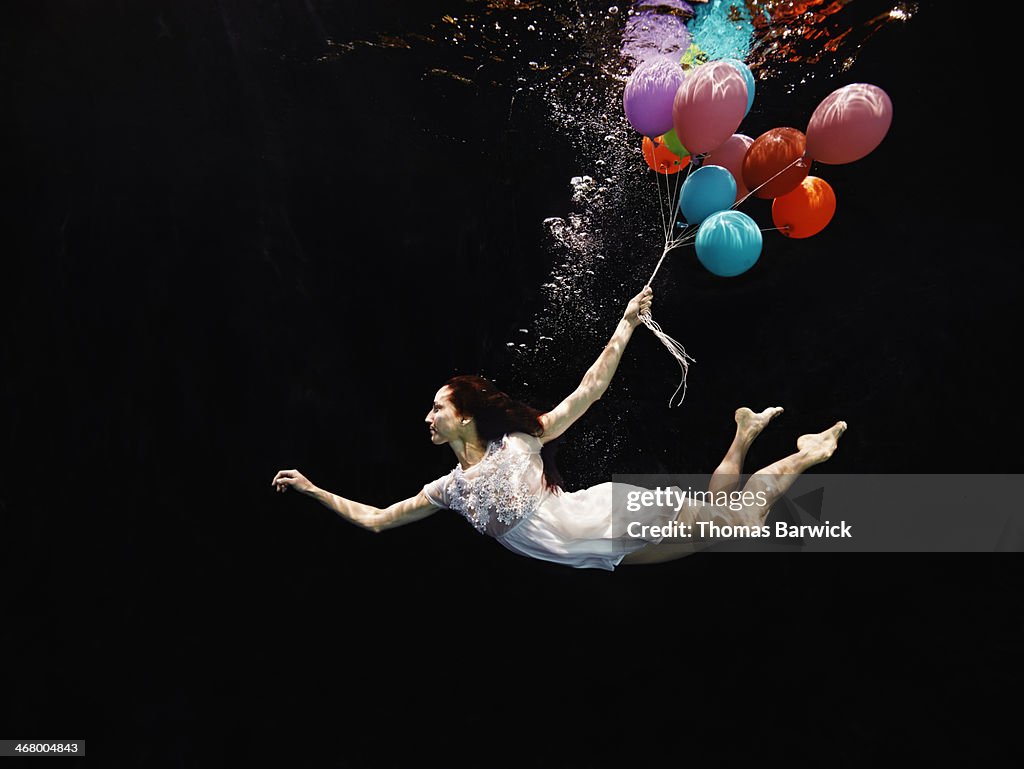 View from underwater of woman holding balloons