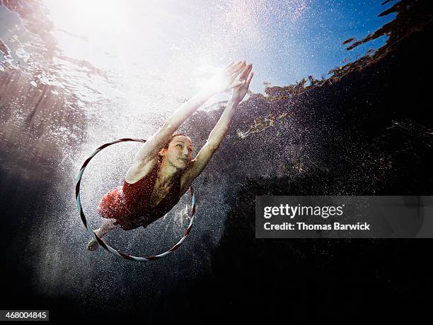 underwater view of woman diving through hoop - moeiteloos stockfoto's en -beelden