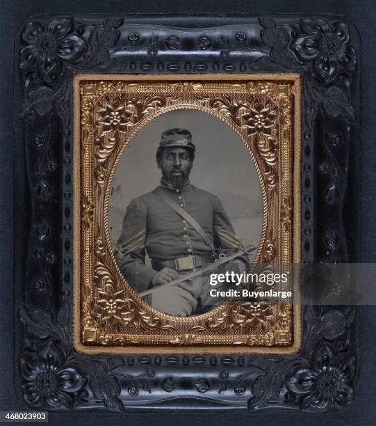 Daguerreotype of an African-American soldier in Union cavalry uniform with cavalry saber in front of painted backdrop showing landscape, 1863.