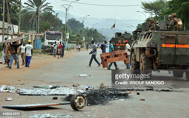 French soldiers of the Sangaris military operation drive past on February 9, 2014 as looters carry items gathered from nearby homes near the site...