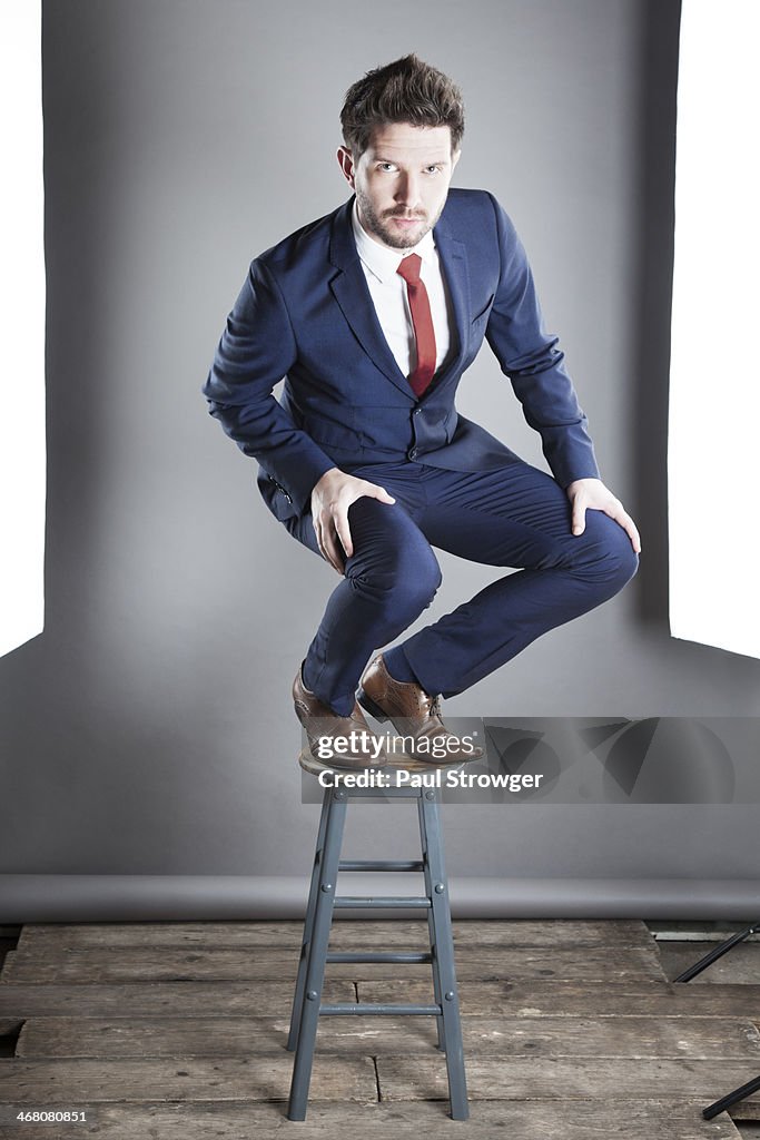 Self, blue suit on stool.