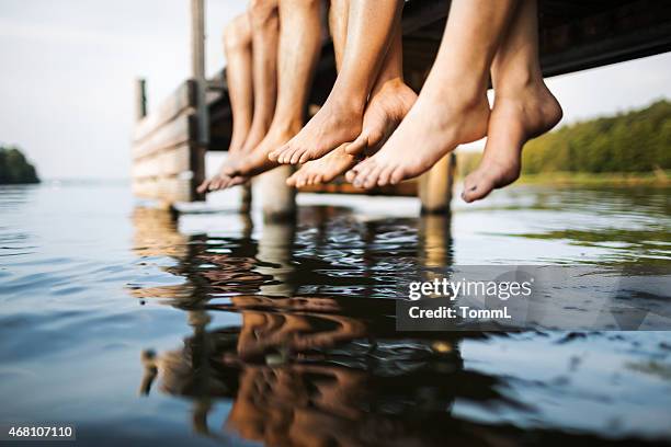 three people sitting on a jetty - male feet pics stockfoto's en -beelden