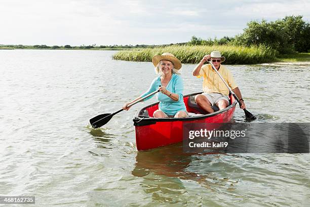 senior couple paddling canoe with oars - seniors canoeing stock pictures, royalty-free photos & images