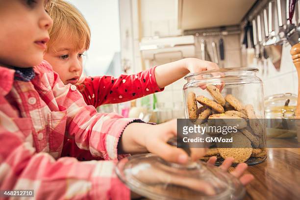 little girls taking oatmeal cookies from a jar - child cookie jar stock pictures, royalty-free photos & images
