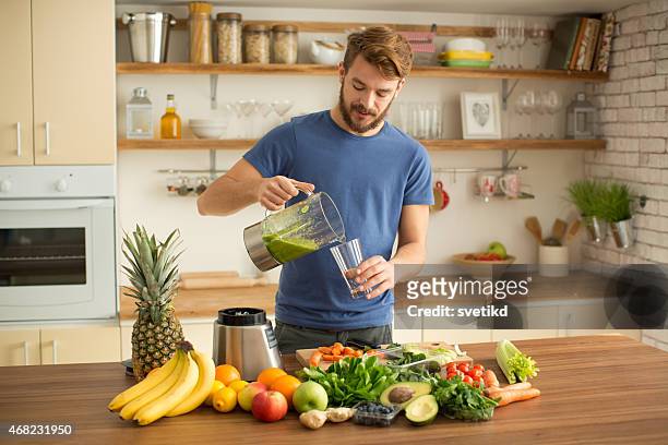 young man making juice or smoothie in kitchen. - fruit smoothie stock pictures, royalty-free photos & images