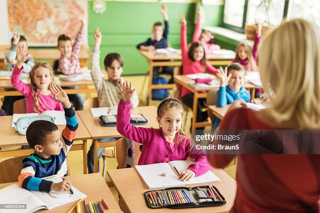 School children raising their hands ready to answer the question.