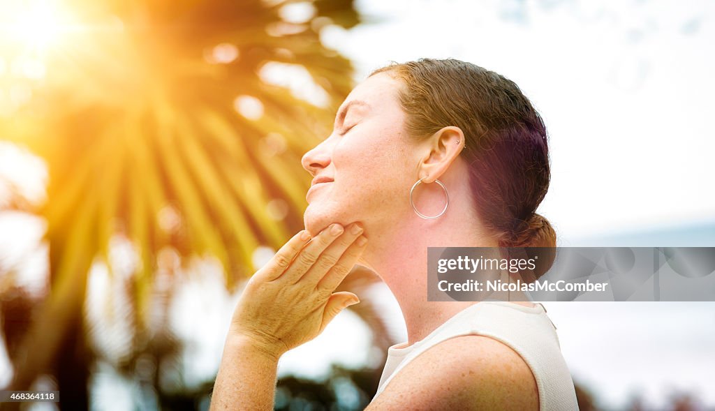 Mid-adult woman applies lotion to her face outdoors profile