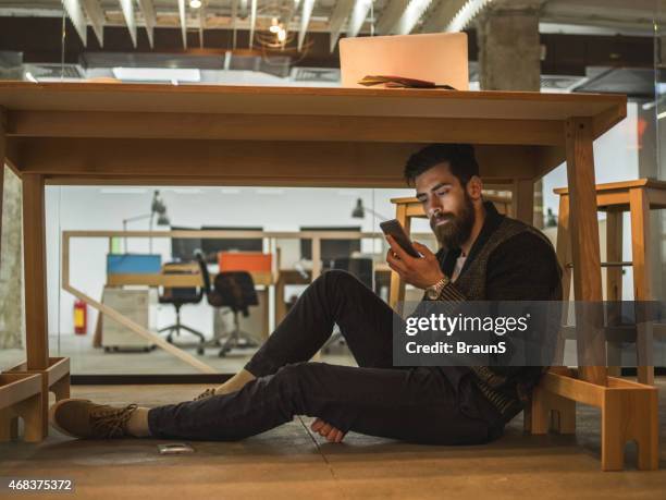 man sitting under the table and using mobile phone. - hide stockfoto's en -beelden