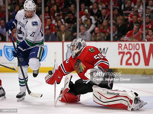 Corey Crawford of the Chicago Blackhawks makes a save next to Daniel Sedin of the Vancouver Canucks at the United Center on April 2, 2015 in Chicago,...