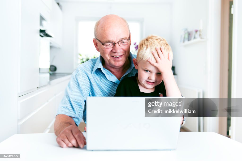 Boy shakes his head working with laptop and granddad