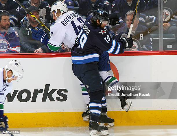 Jim Slater of the Winnipeg Jets checks Sven Baertschi of the Vancouver Canucks into the boards during second period action on April 4, 2015 at the...