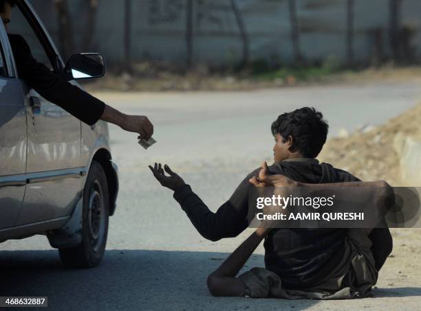 Pakistani beggar who has been affected by polio receives money from a commuter on a street in Islamabad on February 11, 2014. Pakistan is one of only...