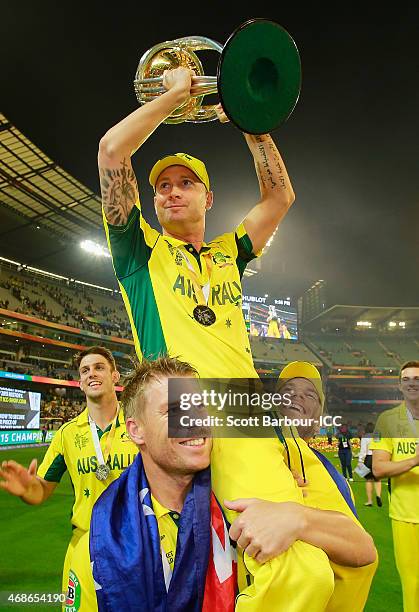 Australian captain Michael Clarke is lifted up by teamates David Warner and Aaron Finch as he holds the World Cup trophy aloft as they celebrate...