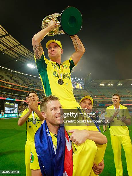 Australian captain Michael Clarke is lifted up by teamates David Warner and Aaron Finch as he holds the World Cup trophy aloft as they celebrate...