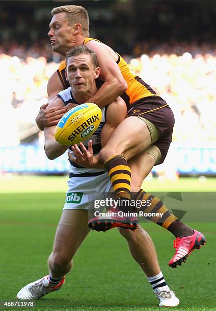 Joel Selwood of the Cats handballs whilst being tackled by Sam Mitchell of the Hawks during the round one AFL match between the Hawthorn Hawks and...