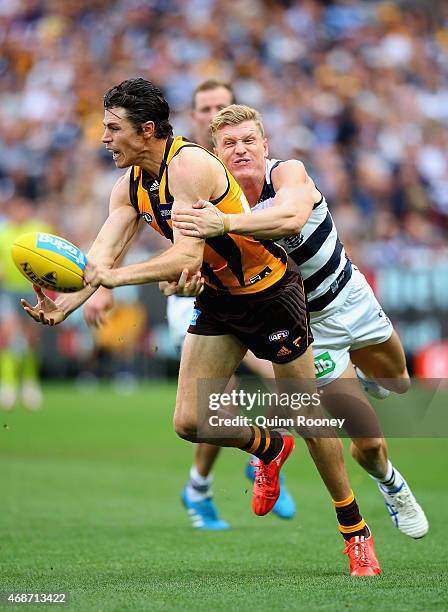 Isaac Smith of the Hawks handballs whilst being tackled by Josh Caddy of the Cats during the round one AFL match between the Hawthorn Hawks and the...