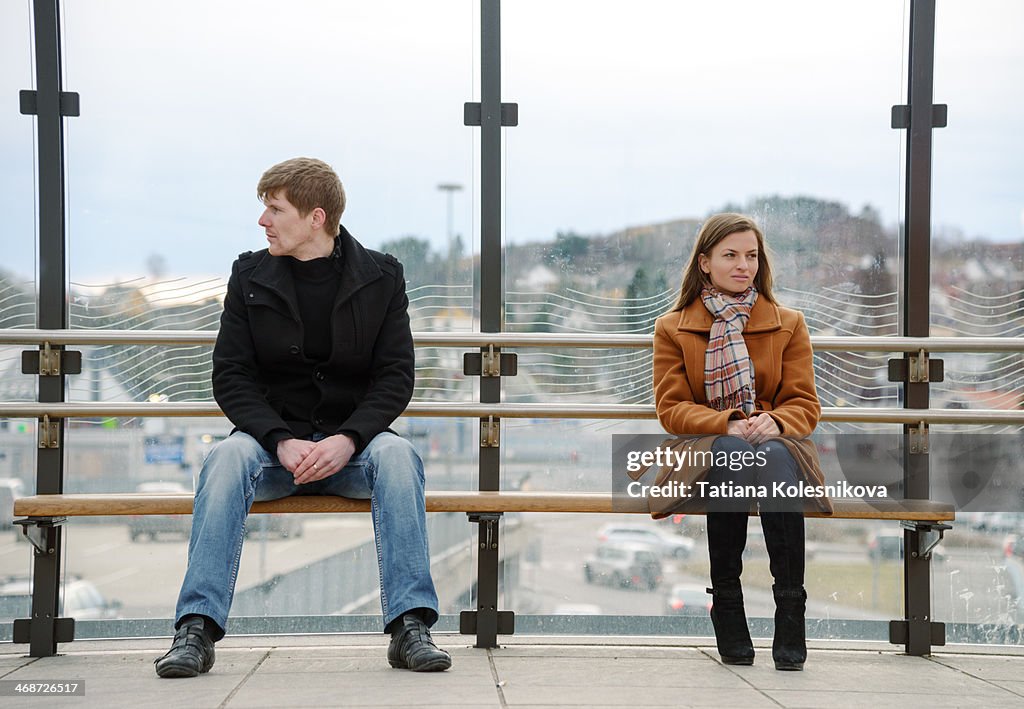 Man amd woman sitting far apart on a bench.