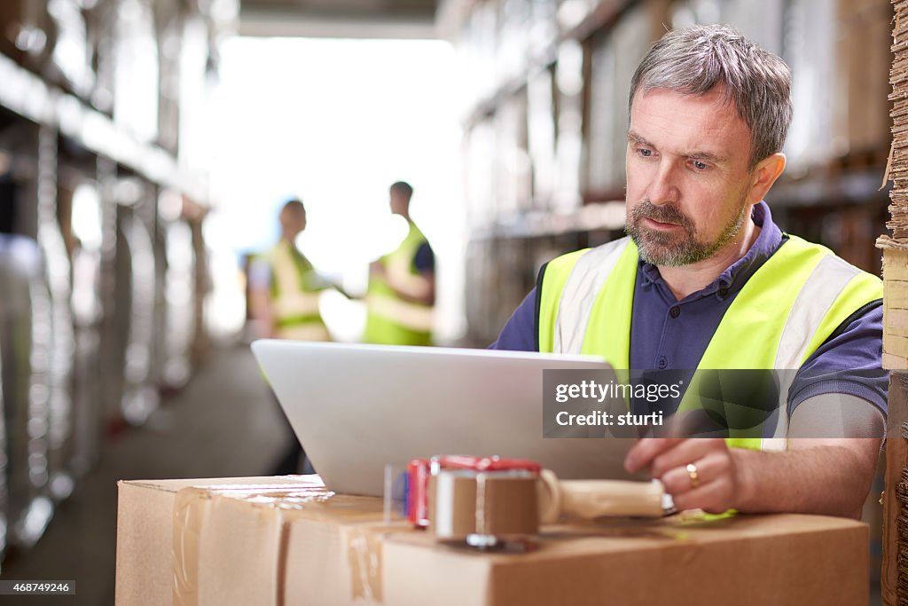 Warehouse manager checking deliveries on his laptop