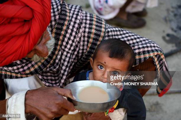 In this photograph taken on March 25 Indian nomadic shepherd Padma Ram helps his nine-month-old granddaughter Anu drink tea at his camp in Sikri in...