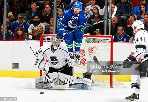 Daniel Sedin of the Vancouver Canucks leaps to avoid the puck in front of Jonathan Quick and Robyn Regehr of the Los Angeles Kings during their NHL...