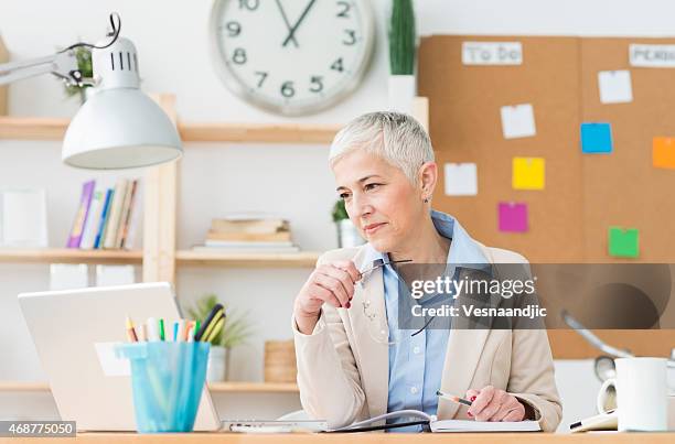 wunderschöne fröhlich reife frau, die auf computer im büro arbeiten - clock person desk stock-fotos und bilder