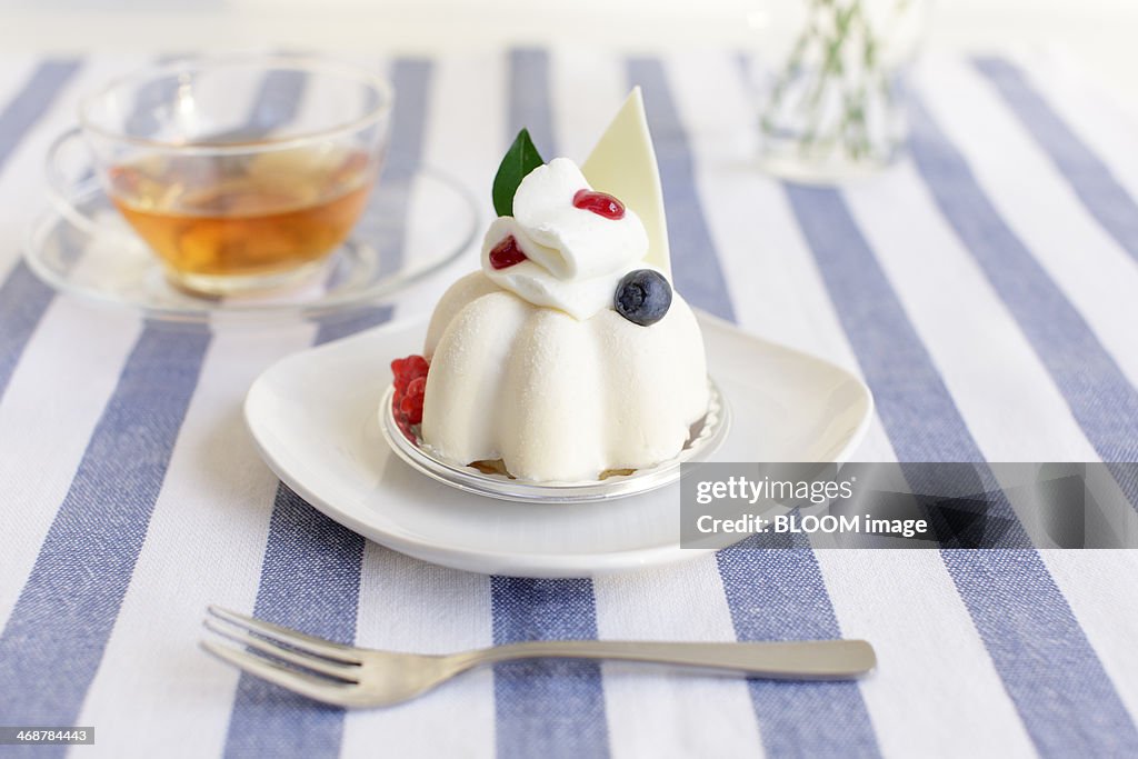 Close-up of white cake and cup of tea on striped tablecloth