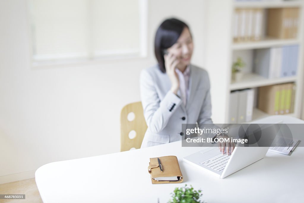 Woman in office, using laptop and talking on phone