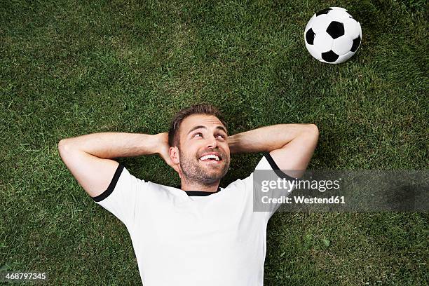 germany, young man lying on lawn looking at football - fan appreciation day stock-fotos und bilder