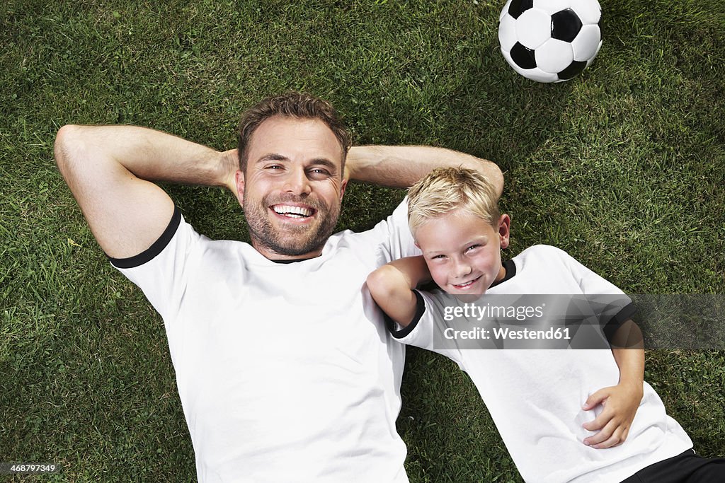 Germany, Father and sun lying on lawn, wearing football shirts